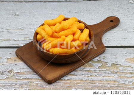 Cheese flavored corn puffs in wooden bowl on rustic wood background, crunchy savory cheese snacks Cheese flavored corn puffs in wooden bowl on rustic wood background, crunchy savory cheese snacks 138833835