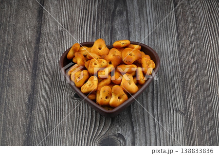 Crispy, flavorful triangular chips in a heart-shaped bowl against a wooden background, a delicious and appetizing food snack. Crispy, flavorful triangular chips in a heart-shaped bowl against a wooden background, a delicious and appetizing food snack. 138833836