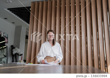 Young woman sitting calmly in front of vertical wood slats in modern office waiting area. Sitting, calmly, waiting, office, young woman. Young woman sitting calmly in front of vertical wood slats in modern office waiting area. Sitting, calmly, waiting, office, young woman. 138833994