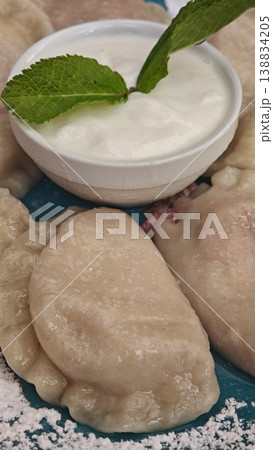 Pierogi arranged on a blue plate accompanied by a bowl of yogurt topped with mint leaves, with powdered sugar sprinkled around for decoration 138834205