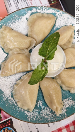 Pierogi served on a turquoise plate, arranged in a circular formation with a bowl of cream and fresh mint in the center, dusted with powdered sugar Pierogi served on a turquoise plate, arranged in a circular formation with a bowl of cream and fresh mint in the center, dusted with powdered sugar 138834206