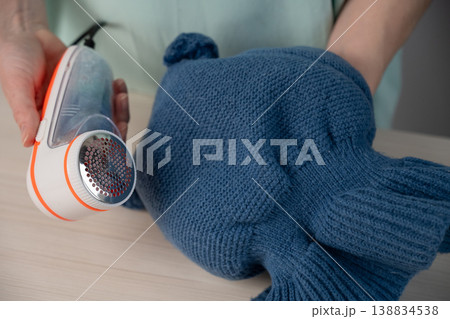 A woman refreshes the look of a child's knitted hat with lint remover. 138834538