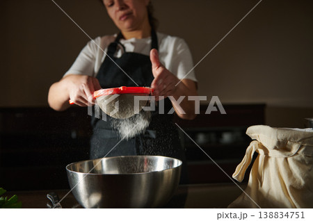 Woman sifting flour into bowl while preparing homemade dough in kitchen 138834751