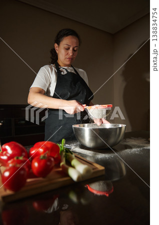 Woman sifting flour into bowl while cooking at home kitchen 138834754