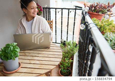 Woman Working on Laptop on Sunny Balcony Surrounded by Potted Plants and Morning Light Woman Working on Laptop on Sunny Balcony Surrounded by Potted Plants and Morning Light 138834794