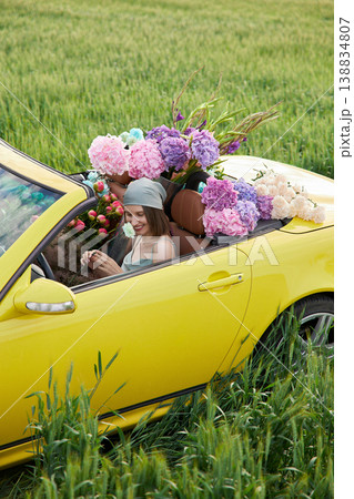 Smiling woman sits in yellow convertible surrounded by colorful flowers 138834807