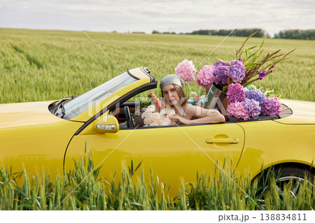 Smiling woman sits in yellow convertible surrounded by colorful flowers Smiling woman sits in yellow convertible surrounded by colorful flowers 138834811