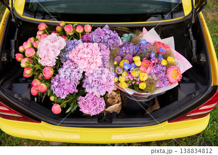 Smiling woman sits in yellow convertible surrounded by colorful flowers 138834812