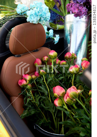 Smiling woman sits in yellow convertible surrounded by colorful flowers Smiling woman sits in yellow convertible surrounded by colorful flowers 138834817