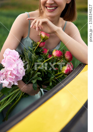 Smiling woman sits in yellow convertible surrounded by colorful flowers Smiling woman sits in yellow convertible surrounded by colorful flowers 138834827