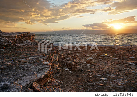 Sun shines through dramatic sunset clouds to waves at Jordanian side of Dead Sea, branches, flotsam, debris and rubbish washed on shore Sun shines through dramatic sunset clouds to waves at Jordanian side of Dead Sea, branches, flotsam, debris and rubbish washed on shore 138835643