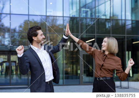 Business colleagues celebrating a successful project achievement, giving a high five with joyful expressions in front of a modern office building, symbolizing teamwork and partnership Business colleagues celebrating a successful project achievement, giving a high five with joyful expressions in front of a modern office building, symbolizing teamwork and partnership 138835755