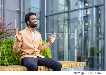 Young man finding inner peace and mindful balance by meditating outdoors in a modern urban environment, integrating relaxation techniques into a busy lifestyle Young man finding inner peace and mindful balance by meditating outdoors in a modern urban environment, integrating relaxation techniques into a busy lifestyle 138835879