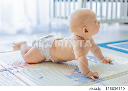 Baby lying on play mat learning to crawl and get on all fours. Infant practicing motor skills and development at home. Early childhood growth, milestones and active learning concept Baby lying on play mat learning to crawl and get on all fours. Infant practicing motor skills and development at home. Early childhood growth, milestones and active learning concept 138836150