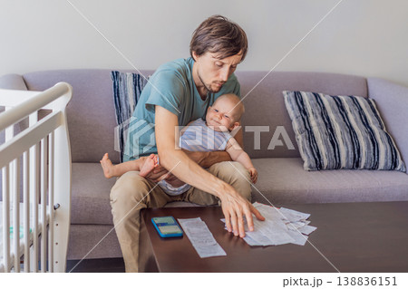 Father sitting on sofa holding baby while calculating monthly expenses with receipts at home. Stressed dad managing budget and childcare. Financial stress, parenthood and real life concept 138836151