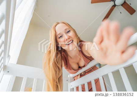 Mother looking into baby crib and playing with newborn at home. Loving mom bonding with infant, smiling and interacting. Parenting care, early childhood development and emotional connection concept 138836152