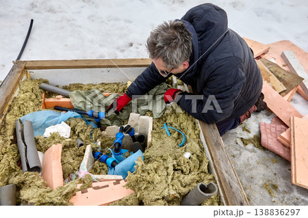 Plumber installing well pit distribution piping in winter in snowy rural area. 138836297