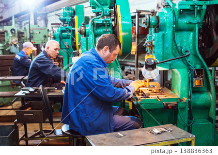 Worker in production plant drilling at machine on the factory floor. Factory Workers at Work. Workers operating metal processing machines at workshop. 138836363