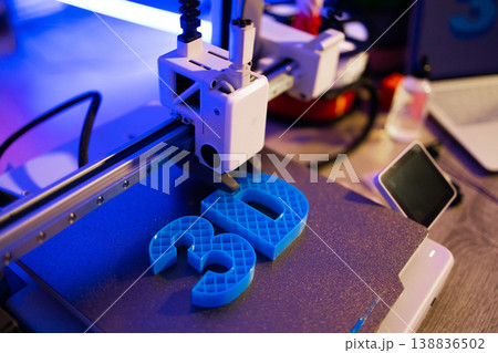 A modern 3D printer is actively creating bright blue letters on a textured build plate with vibrant blue and purple lighting A modern 3D printer is actively creating bright blue letters on a textured build plate with vibrant blue and purple lighting 138836502