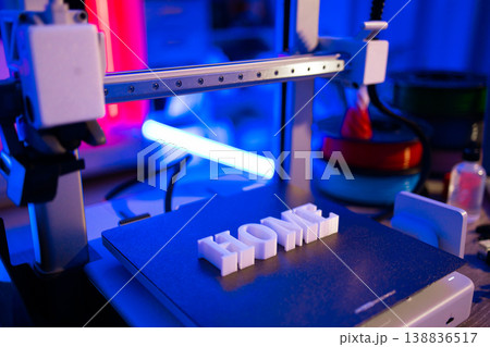 A 3D printer is actively creating the word HOME in white letters on its build plate with colorful ambient lighting 138836517