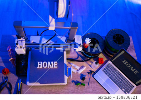 A 3D printer is set up with filament spools and a laptop displaying the word HOME, suggesting a home-based creative project 138836521
