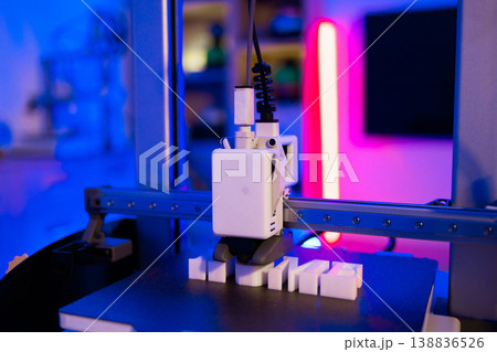 A modern 3D printer is actively creating white letters on a black platform with vibrant blue and pink lighting A modern 3D printer is actively creating white letters on a black platform with vibrant blue and pink lighting 138836526