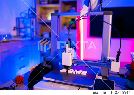 A modern 3D printer is actively creating the word HOME in white plastic letters on its build plate, illuminated by vibrant blue and pink neon lights 138836544
