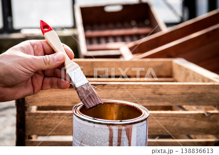 Hand Holding Brush Dipping Into Wood Stain for Crate Restoration 138836613