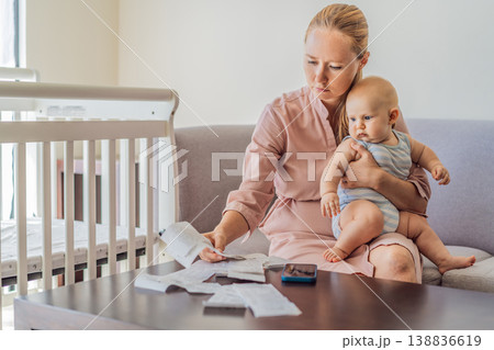 Mother sitting on sofa holding baby while calculating monthly expenses with receipts at home. Stressed mom managing budget and childcare. Financial stress, parenthood and real life concept Mother sitting on sofa holding baby while calculating monthly expenses with receipts at home. Stressed mom managing budget and childcare. Financial stress, parenthood and real life concept 138836619