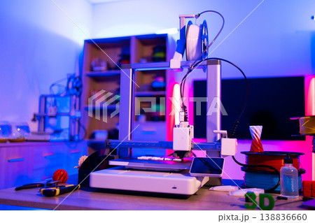 A modern 3D printer is actively creating an object in a workshop illuminated by vibrant blue and pink neon lights, showcasing innovation and technology 138836660