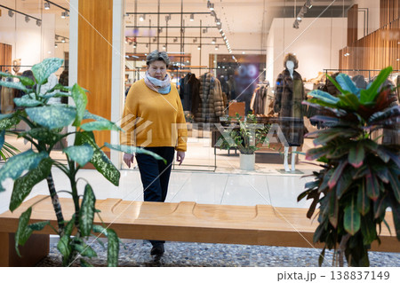 Mature woman walking in modern shopping mall near clothing store window Mature woman walking in modern shopping mall near clothing store window 138837149
