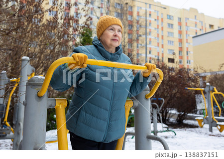 Senior woman exercising on outdoor fitness machine in winter Senior woman exercising on outdoor fitness machine in winter 138837151