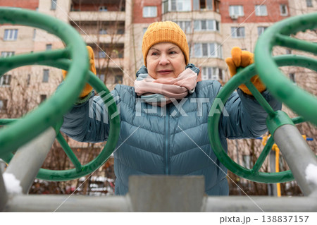 Senior woman exercising on outdoor fitness machine in winter Senior woman exercising on outdoor fitness machine in winter 138837157