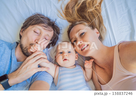 Baby lying with mother and father on bed at home. Loving family relaxing together, enjoying bonding and closeness. Parenthood, tenderness, comfort and emotional connection concept Baby lying with mother and father on bed at home. Loving family relaxing together, enjoying bonding and closeness. Parenthood, tenderness, comfort and emotional connection concept 138837246
