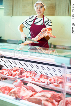 Young saleswoman cutting fresh lamb carcass at counter in butcher store 138839307