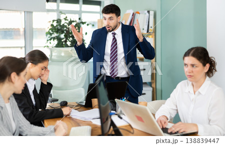 Young man standing and scolding sad seated colleagues in office 138839447