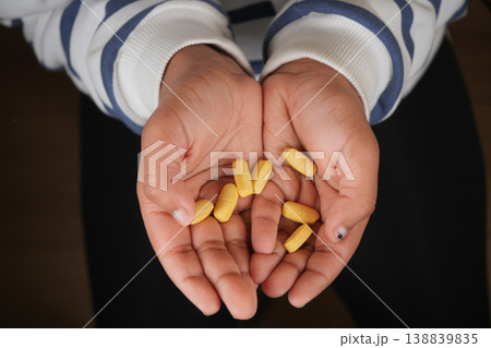 child hands hold yellow pills in a indoor setting 138839835