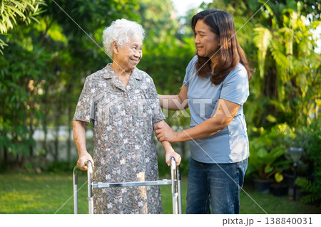 Caregiver help Asian elderly woman patient walk with walker in park. 138840031