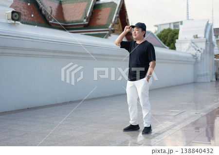 A traveler pauses beside a cultural landmark, taking in the moment with a relaxed and curious attitude. His casual posture reflects the joy of exploring new places on a warm day. A traveler pauses beside a cultural landmark, taking in the moment with a relaxed and curious attitude. His casual posture reflects the joy of exploring new places on a warm day. 138840432