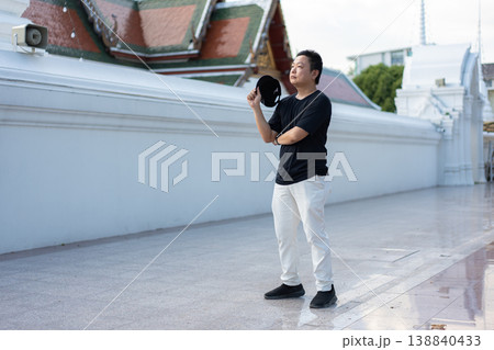 A traveler pauses beside a cultural landmark, taking in the moment with a relaxed and curious attitude. His casual posture reflects the joy of exploring new places on a warm day. A traveler pauses beside a cultural landmark, taking in the moment with a relaxed and curious attitude. His casual posture reflects the joy of exploring new places on a warm day. 138840433