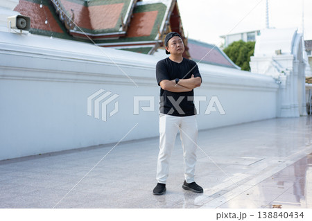 A traveler pauses beside a cultural landmark, taking in the moment with a relaxed and curious attitude. His casual posture reflects the joy of exploring new places on a warm day. A traveler pauses beside a cultural landmark, taking in the moment with a relaxed and curious attitude. His casual posture reflects the joy of exploring new places on a warm day. 138840434