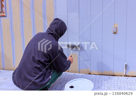 Person paints wall with roller while crouched on exterior walls in construction area Person paints wall with roller while crouched on exterior walls in construction area 138840629