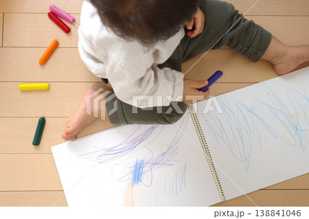 家のフローリングでスケッチブックにクレヨンで絵を描く子供 家のフローリングでスケッチブックにクレヨンで絵を描く子供 138841046