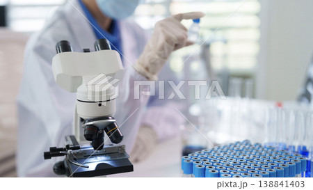 Adult researcher wearing mask examines sample vial with laboratory microscope Scientific discovery medical innovation healthcare technology development Adult researcher wearing mask examines sample vial with laboratory microscope Scientific discovery medical innovation healthcare technology development 138841403