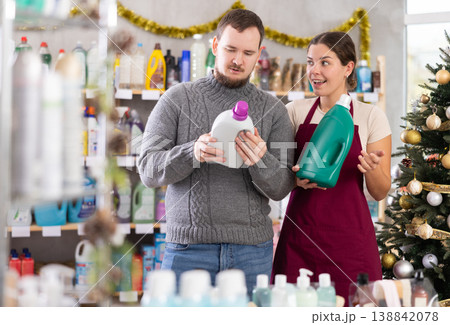 Experienced young female seller offers household liquid detergents to man in store. Christmas shopping 138842078