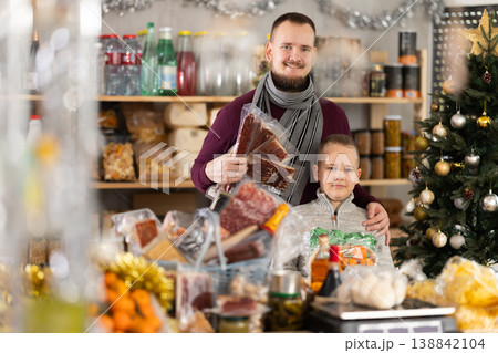 Father and son standing in festive market with chosen products in hands Father and son standing in festive market with chosen products in hands 138842104