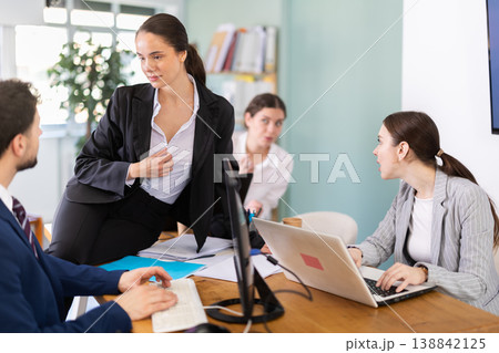 Young woman flirting with male colleague while sitting on office desk 138842125