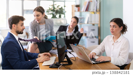 Young woman flirting with male colleague while sitting on office desk 138842181
