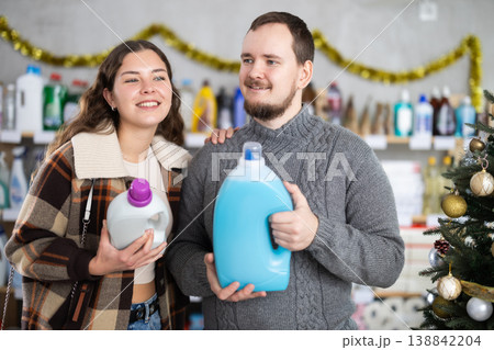 Happy man and woman looking for household liquid detergents on shelves in store. Christmas shopping Happy man and woman looking for household liquid detergents on shelves in store. Christmas shopping 138842204