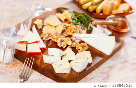 Cheese slices on wooden board with honey, walnuts, arugula Cheese slices on wooden board with honey, walnuts, arugula 138842510